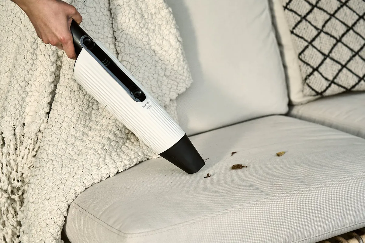 Eine Hand führt den Kobold VM7 über Krümel auf einem hellen Sofa