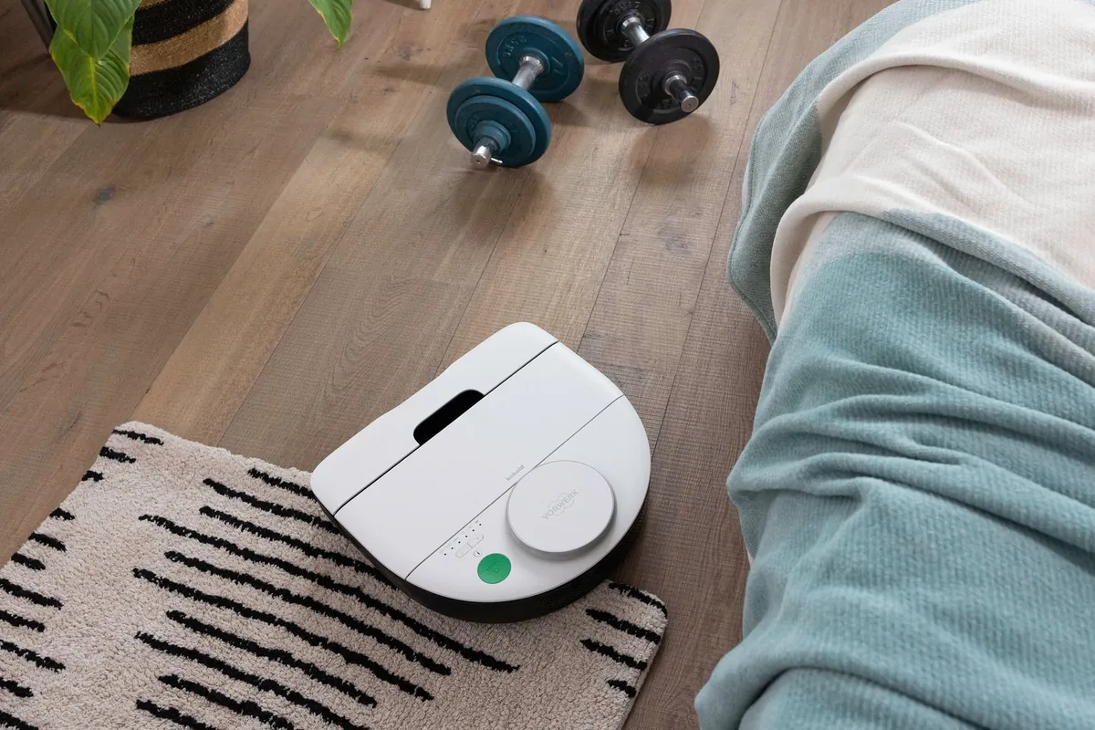 Kobold VR7 fährt neben einem Bett vom Holzboden auf einen Teppich